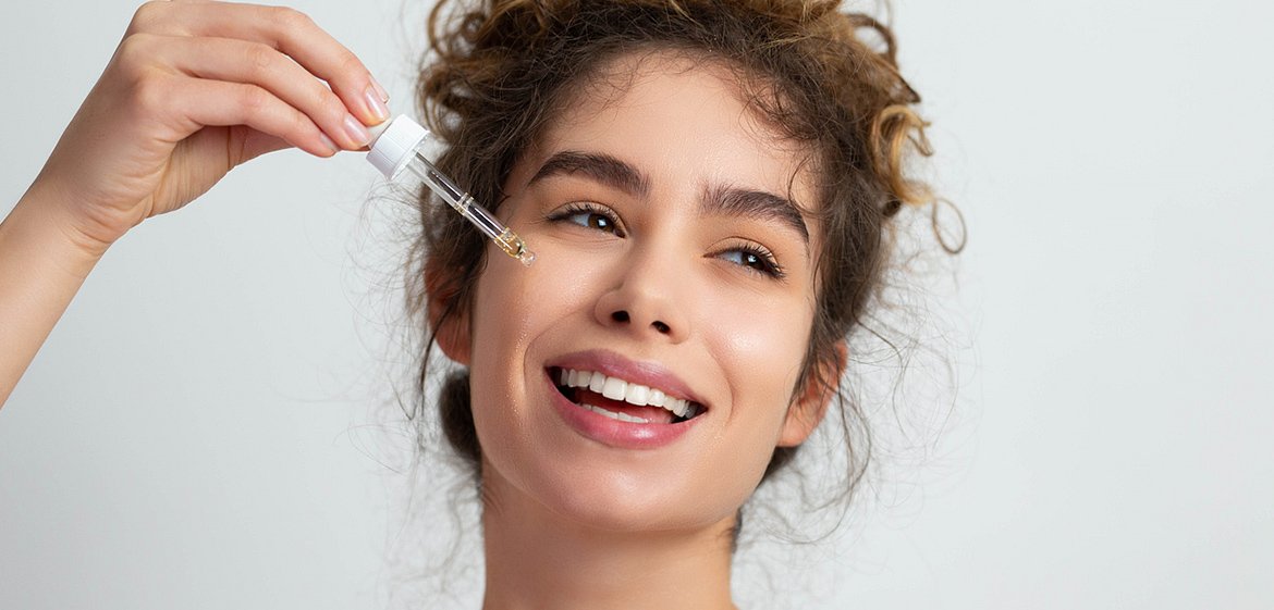 Junge Frau träufelt sich ein Serum mittels Pipette ins Gesicht.